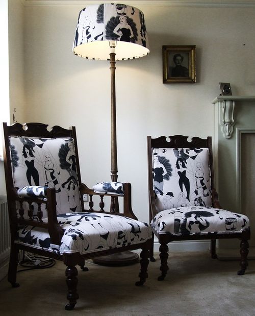 Pair of wooden chairs with black and white patterned cushions in a room with a lamp and wall art.
