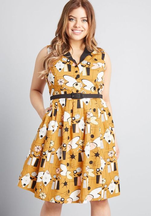 Woman wearing a mustard yellow dress with black and white pattern on a gray background