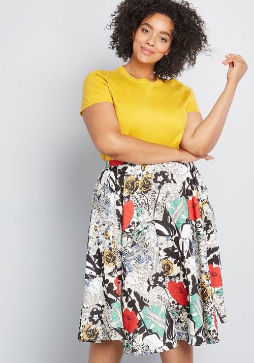 Woman wearing a yellow top and a colorful floral skirt on a light gray background