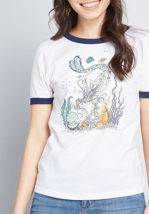 Person wearing a white t-shirt with a colorful mermaid design on a gray background